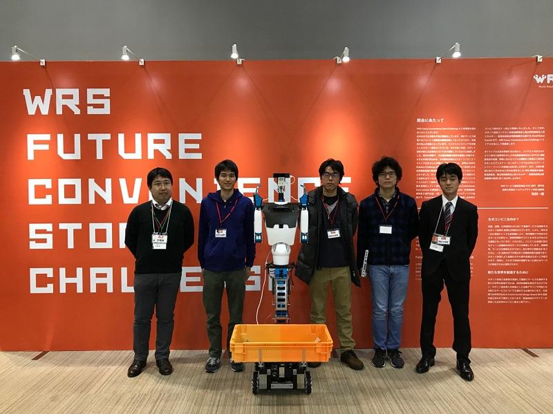 チームメンバーとロボット（WRS Future Convenience Store challengeの看板の前にて）