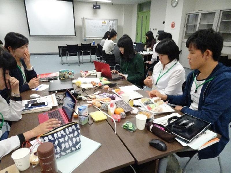 机の上にある患者さんに説明用の食べ物のサンプルをみながらイメージを膨らます多職種の学生達