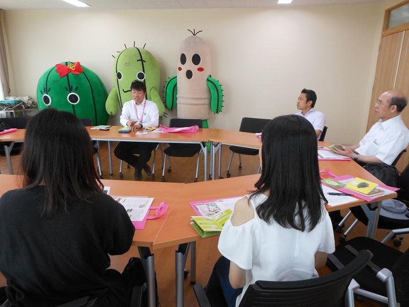 春日井サボテンイメージキャラクターの春代 (はるよ)，日丸 (にちまる)，井之介　(いのすけ) を背にして，春日井サボテンについて説明する高木氏．