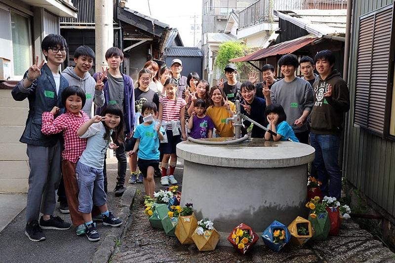 せこ道の井戸端にて。作った植木鉢を飾り、記念撮影をした子ども達と学生。