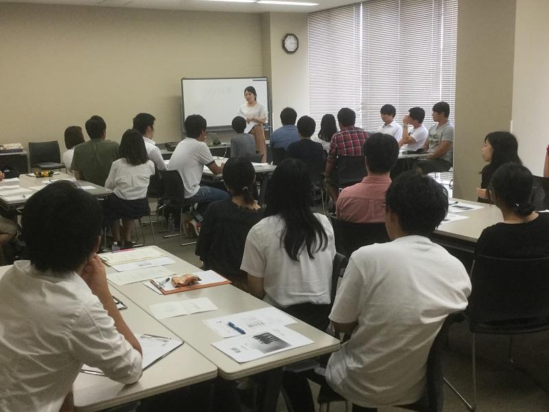 歴代ゼミ長の15分スピーチ；写真は初代ゼミ長・塚本静さんのスピーチ風景。学校現場の苦労話、生徒とのかかわりのほっこりエピソード等、熱い思いが後輩たちに届けられた。