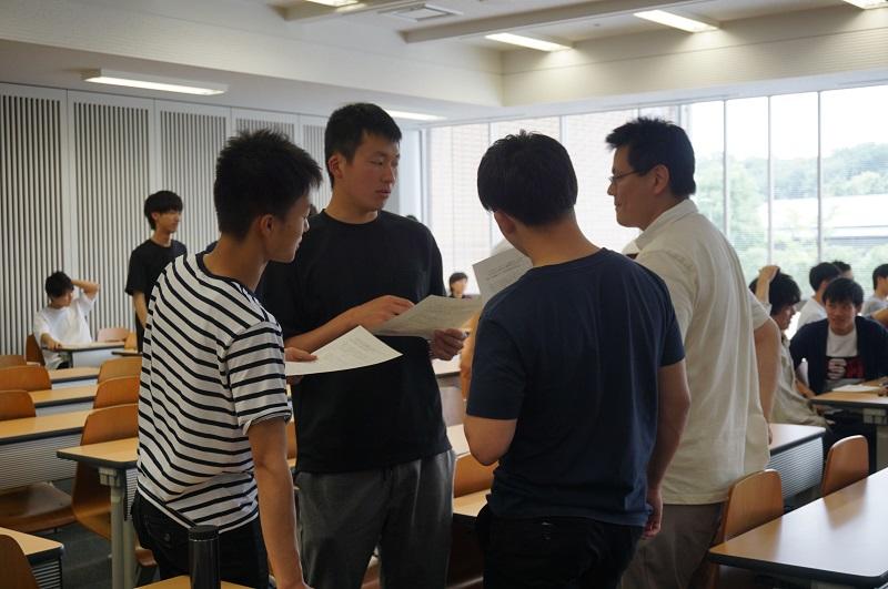 松本教授（右）のアドバイスを受けながら、学生同士で課題の文章を検討