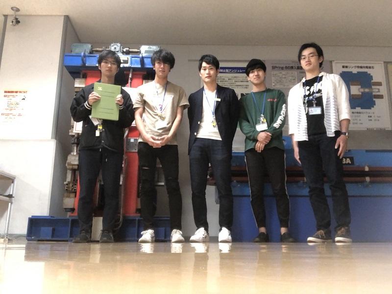 Spring-8のビームラインから出たところにある廊下で撮った写真。後ろにはアンジュレータが展示されている。全員の首から下がっているものはユーザカードで、ビームラインに出入りする際は、自分のユーザカードをタッチしなければならない。