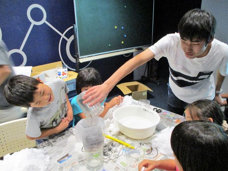 泥水を装置にいれる高校生(写真右)と観察する小学生の様子(写真左)。