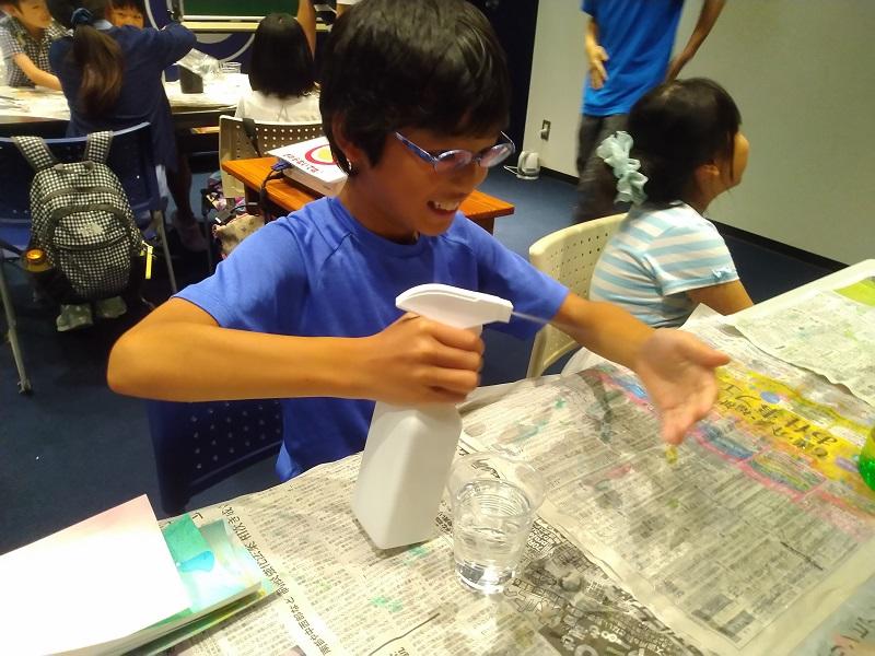 「熱いお湯も霧吹きでひんやりと感じるのか（気化熱）」という実験で本当に冷たく感じるのか試す小学生。