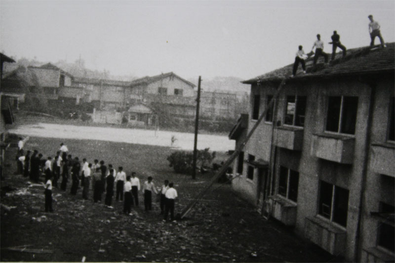 台風一過、窓ガラスが吹き飛んだ駒方校舎の屋根に上がって作業をする学生たち（1959年9月27日）