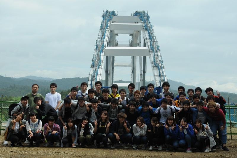 建設中の鶴亀大橋をバックに記念写真に納まる参加者たち=宮城県気仙沼市大島で