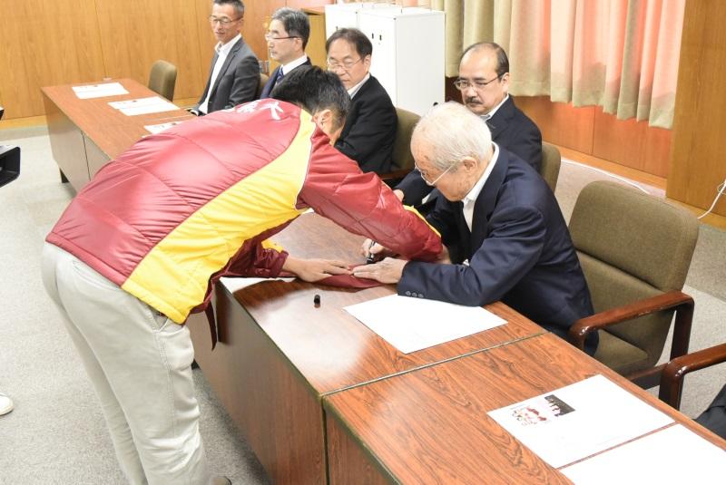 えんじのたすきにサインする小笠原理事長