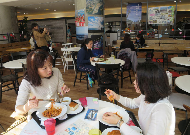 気仙沼の観光ポスターなどが張られた店内で食事をする来場者