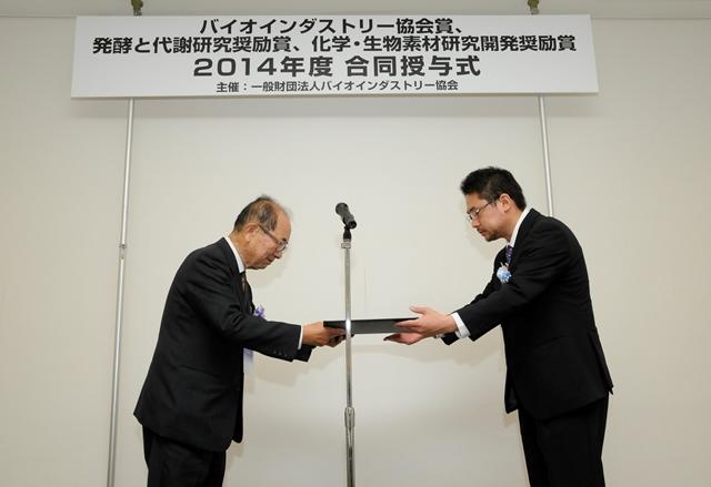 バイオインダストリー協会の大石道夫会長（元日本分子生物学会会長、東京大学名誉教授）から賞状を受け取る志水助教（写真提供：JBA）