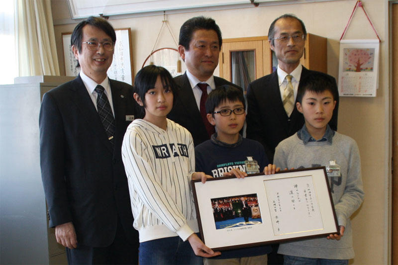 赤﨑終身教授に色紙を手にする児童代表の3人。後列は左から広瀬さん、青山課長、山崎校長