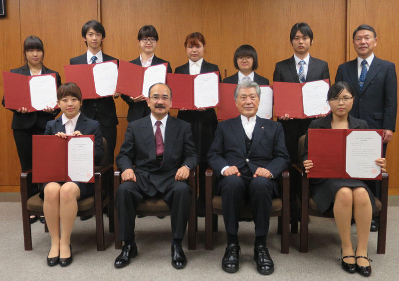 長谷川氏(前列右から2人目)、吉久学長(同3人目)らと記念写真に収まる奨学生8人