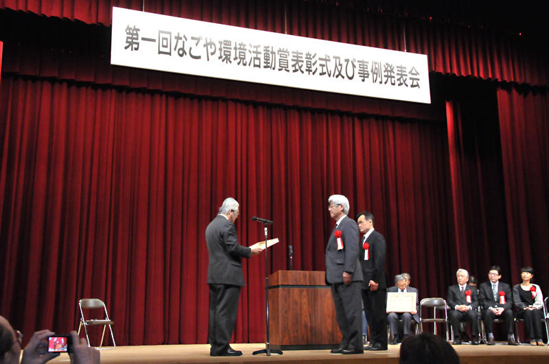 入倉名古屋市副市長から、木製の賞状を受け取る伊藤教授と福井課長