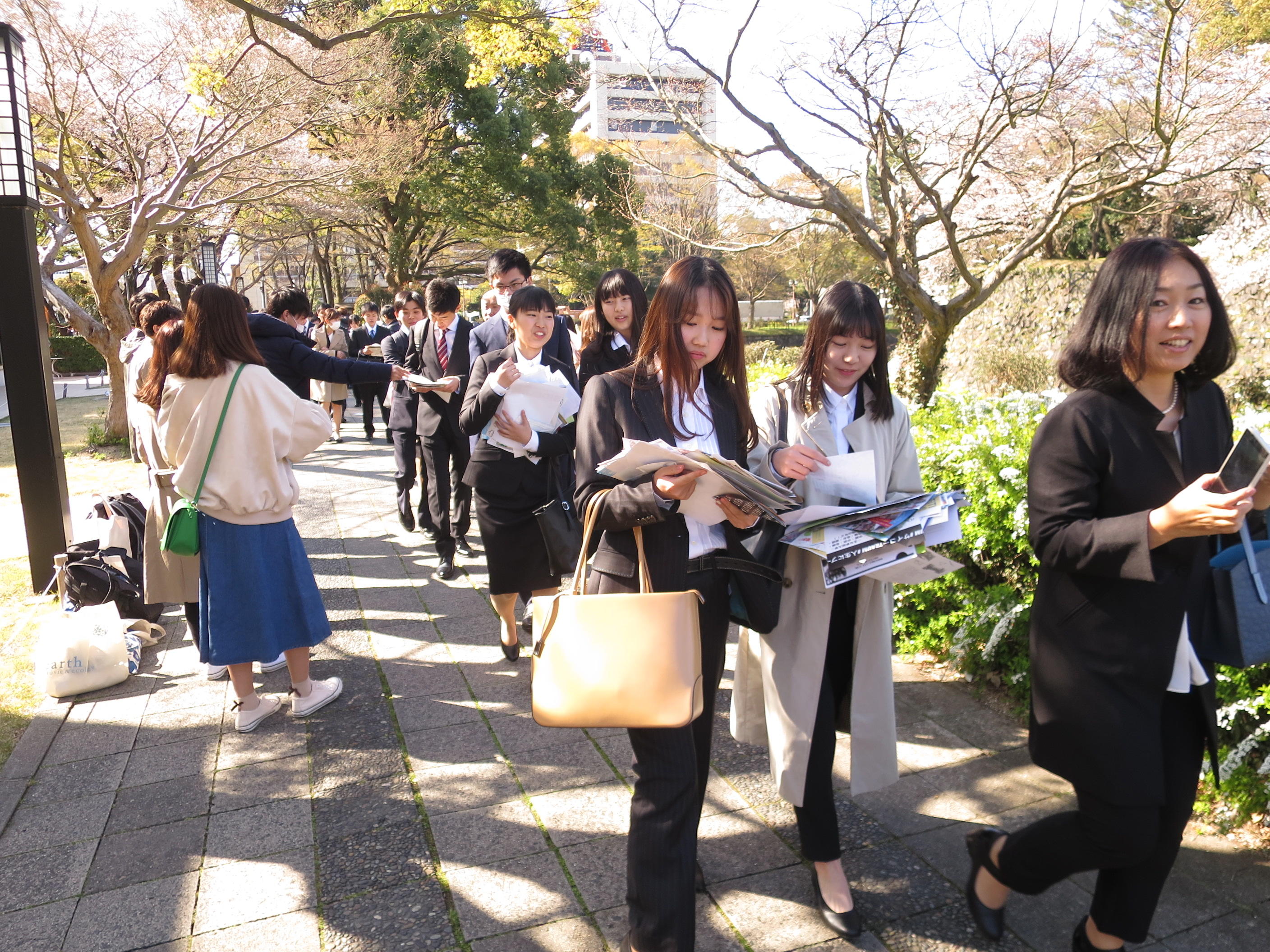 サークル勧誘のチラシをもらいながら入学式場に向かう新入生たち