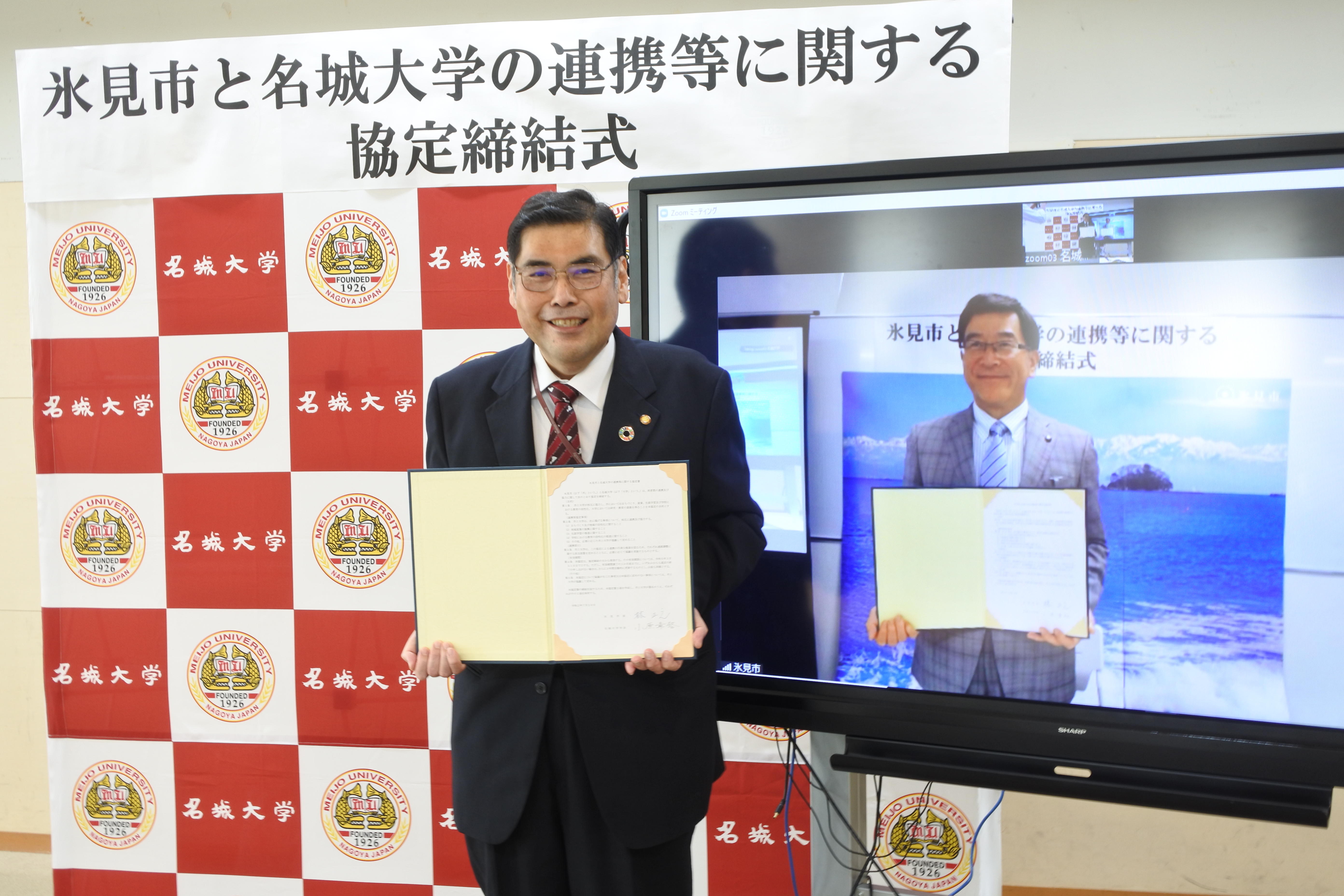 小原章裕学長（左）と林正之氷見市長が互いにモニター画面の相手と一緒に記念撮影