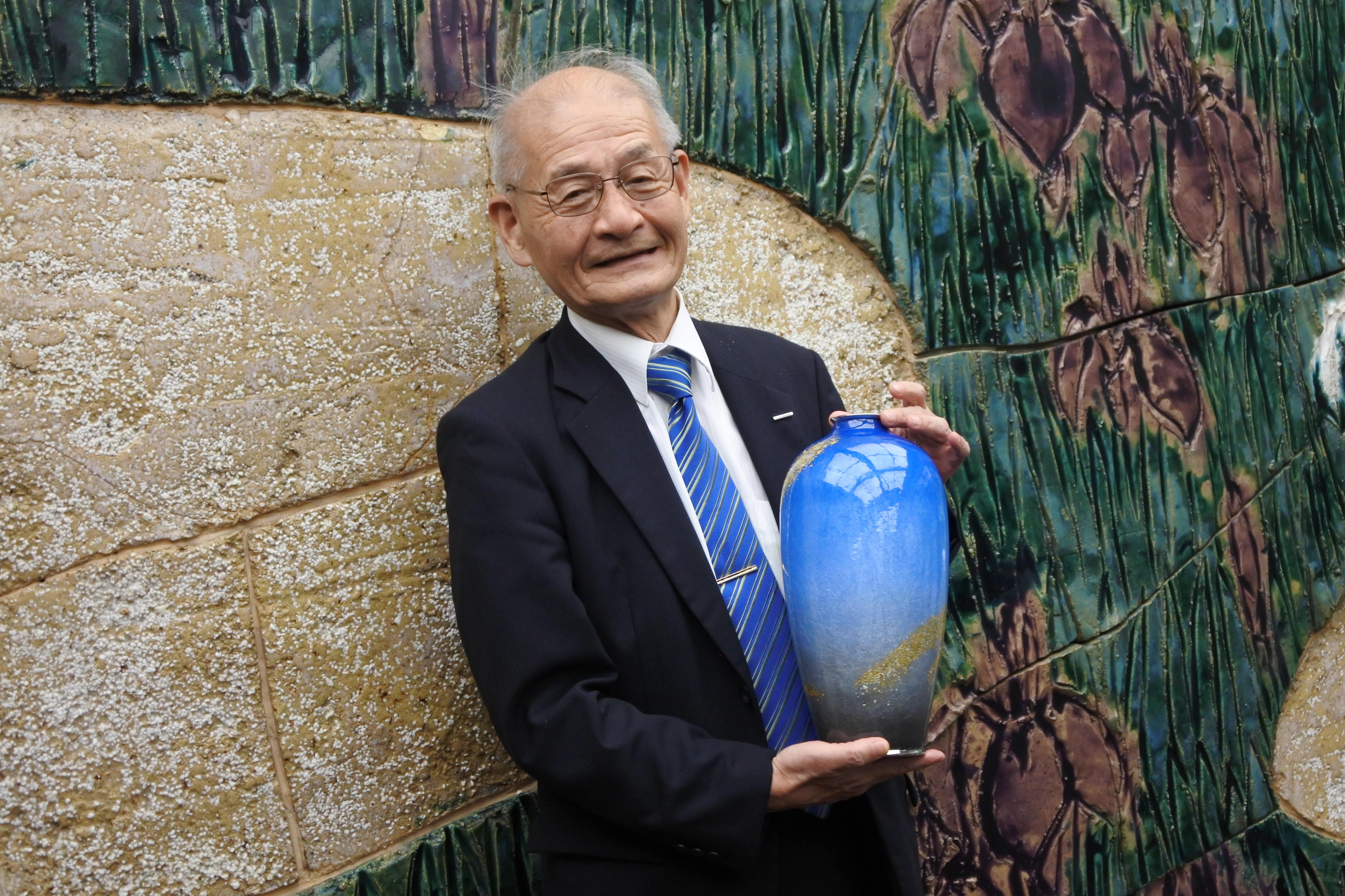 記念品の七宝花瓶を手にいつもの笑顔で記者の質問に答える吉野教授