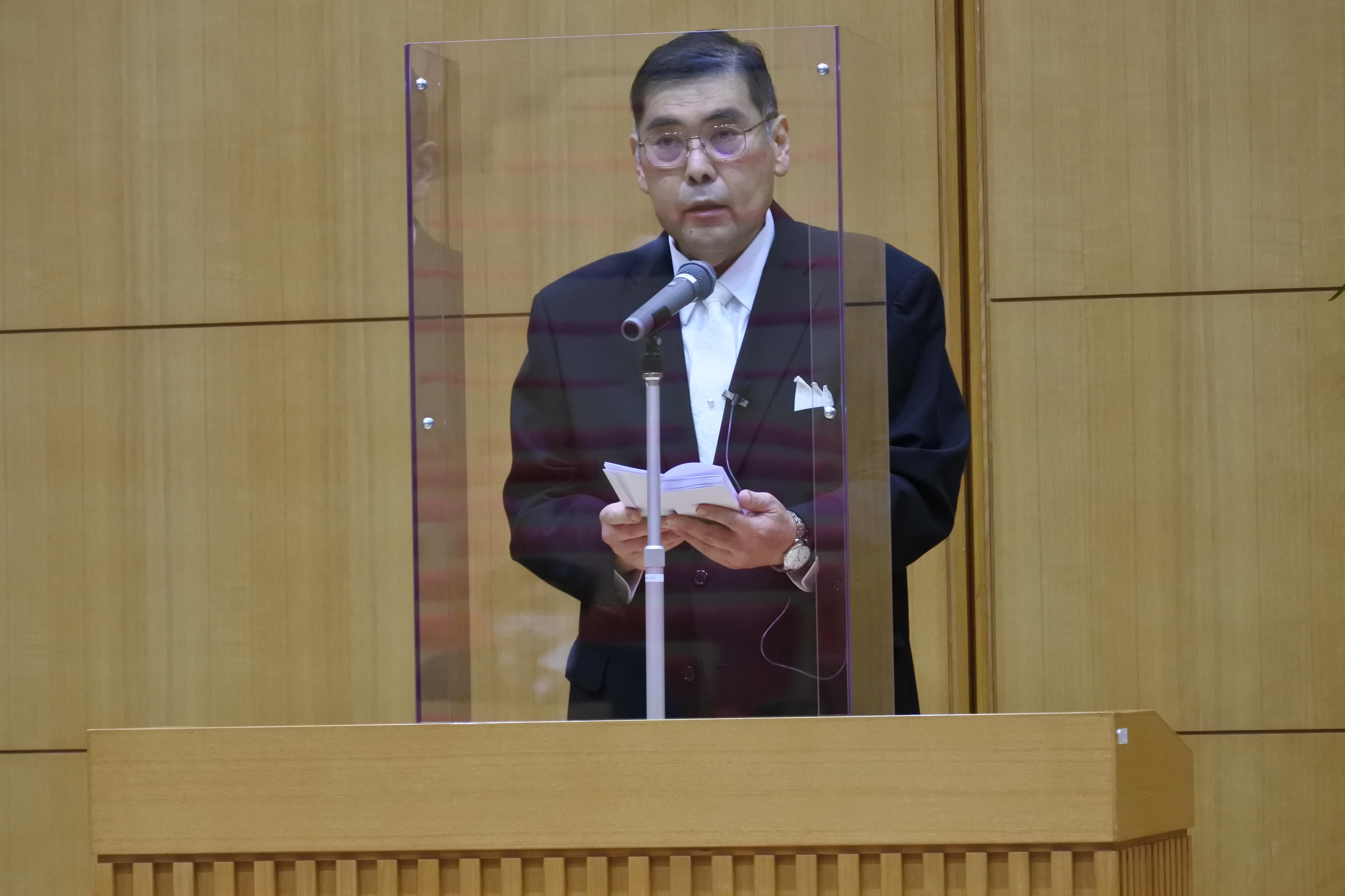 アクリル板を前に告辞を読む小原章裕学長