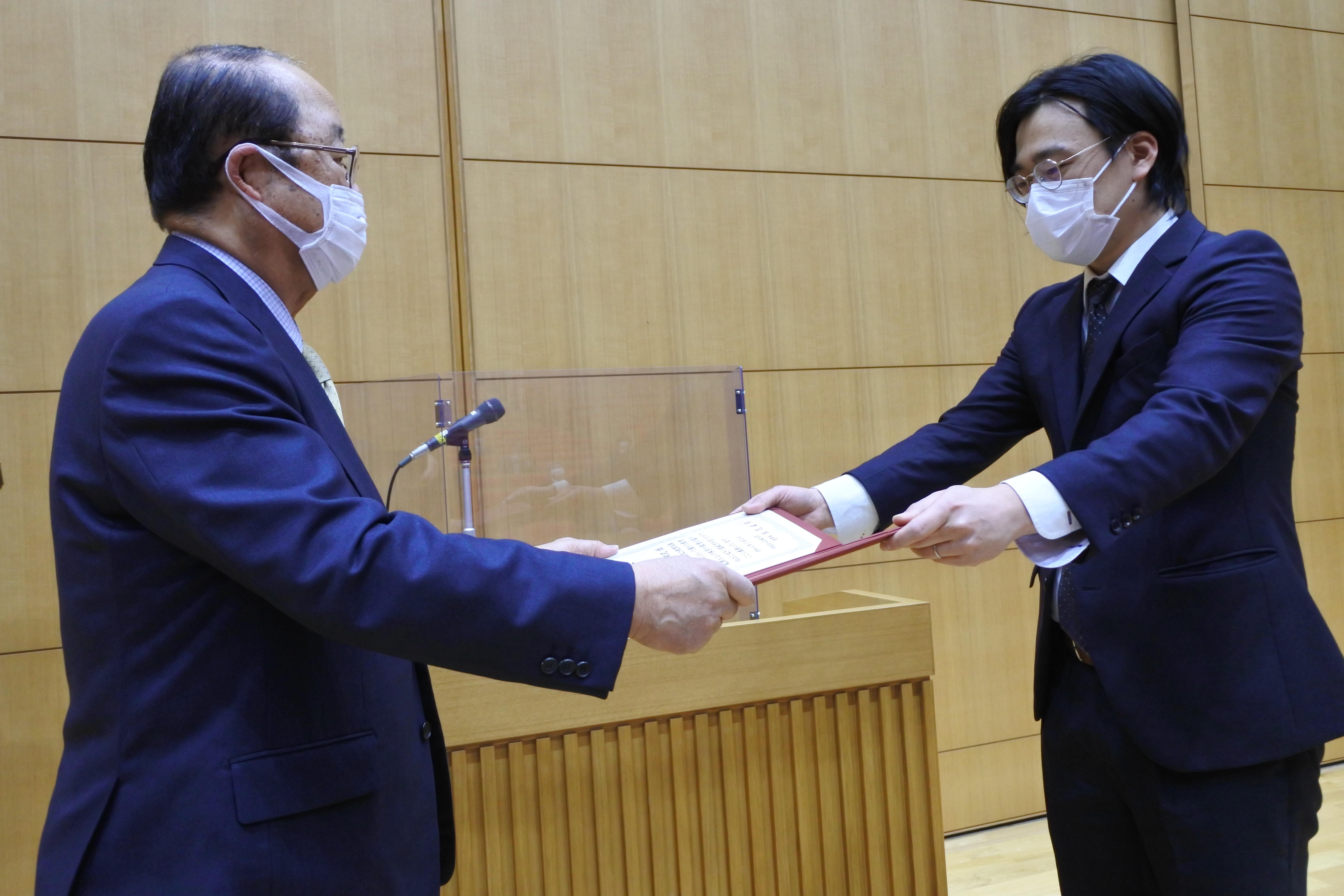 立花貞司理事長（左）から表彰状を受け取る佐藤布武助教