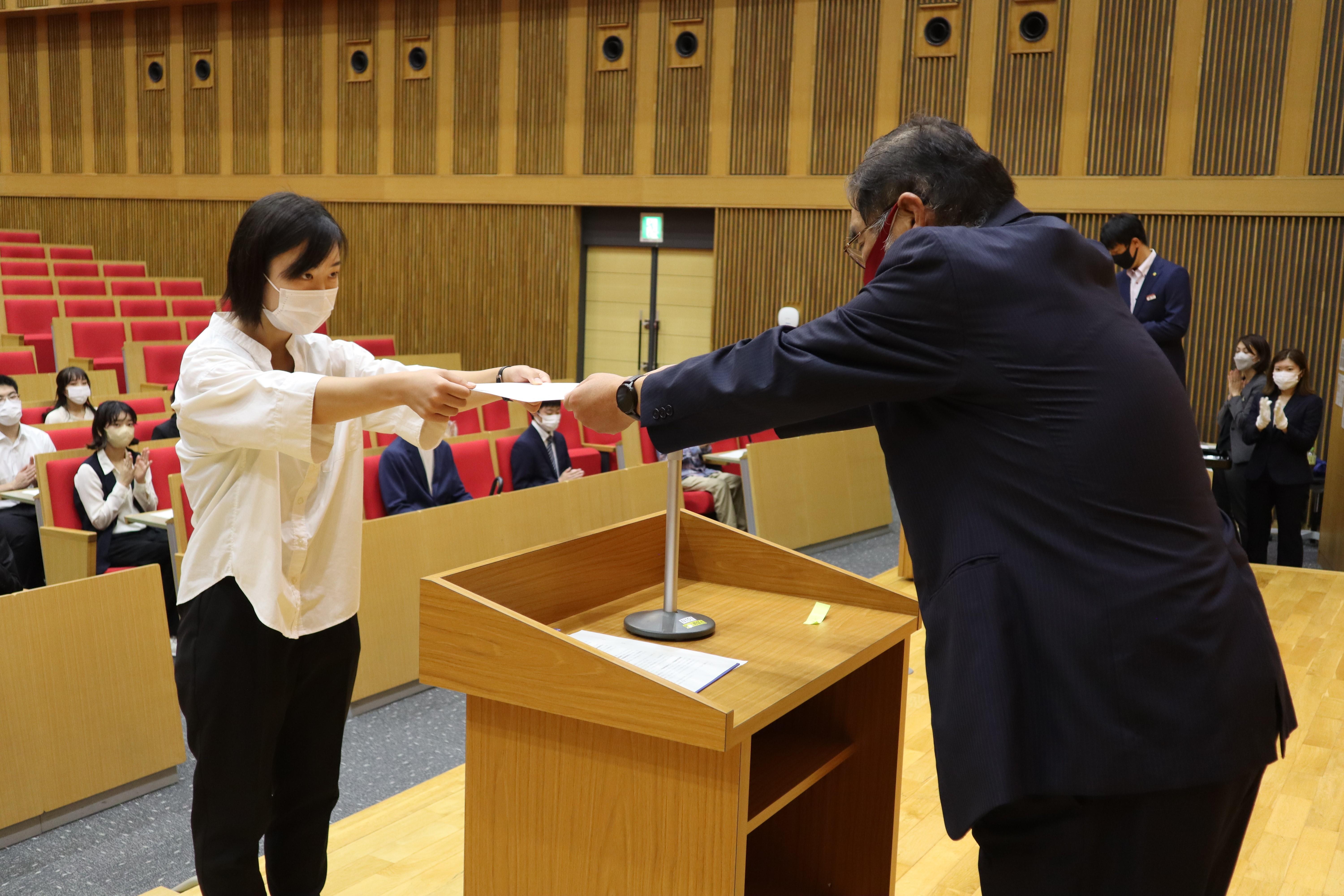 小原学長（右）から学業優秀奨学生の決定通知書を受ける増田佳那さん