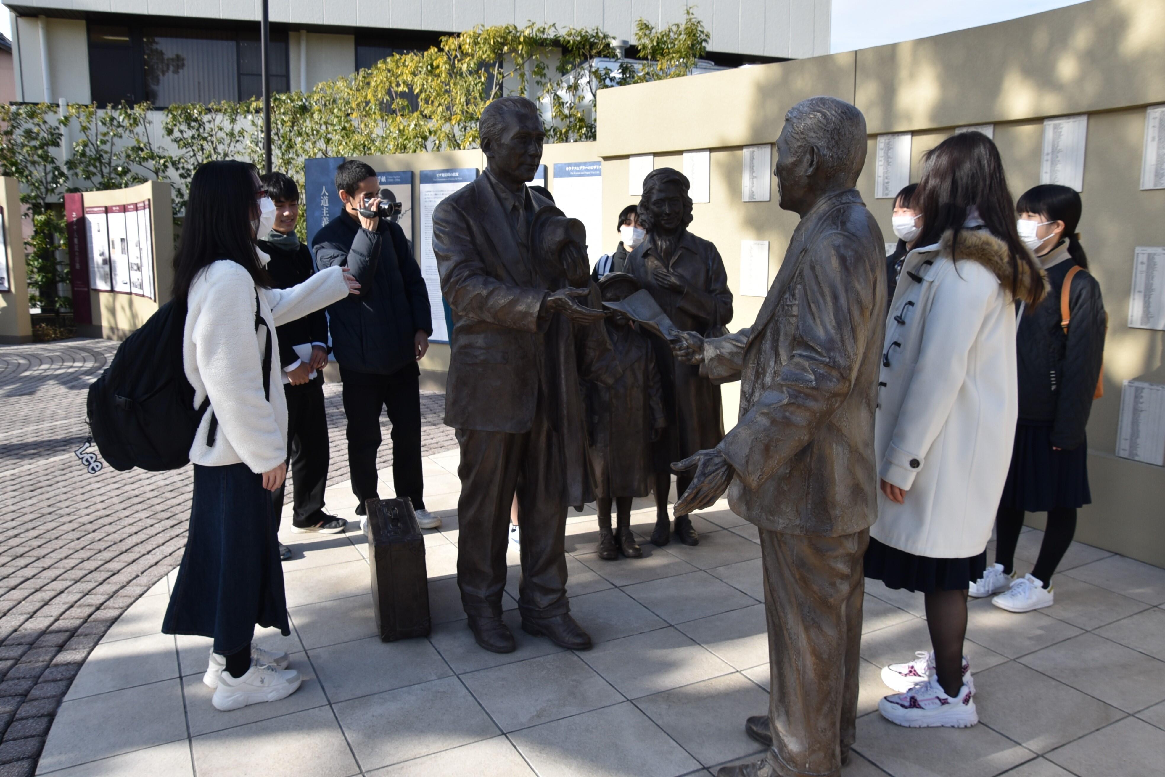 千畝とユダヤ人家族を表現したブロンズ像の前で香川県の高校生をガイドする東條さん（左端）