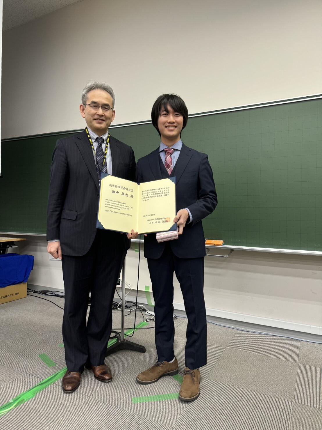 グループを代表して賞状を受け取る田中さん（右）と、応用物理学会の木本恒暢会長