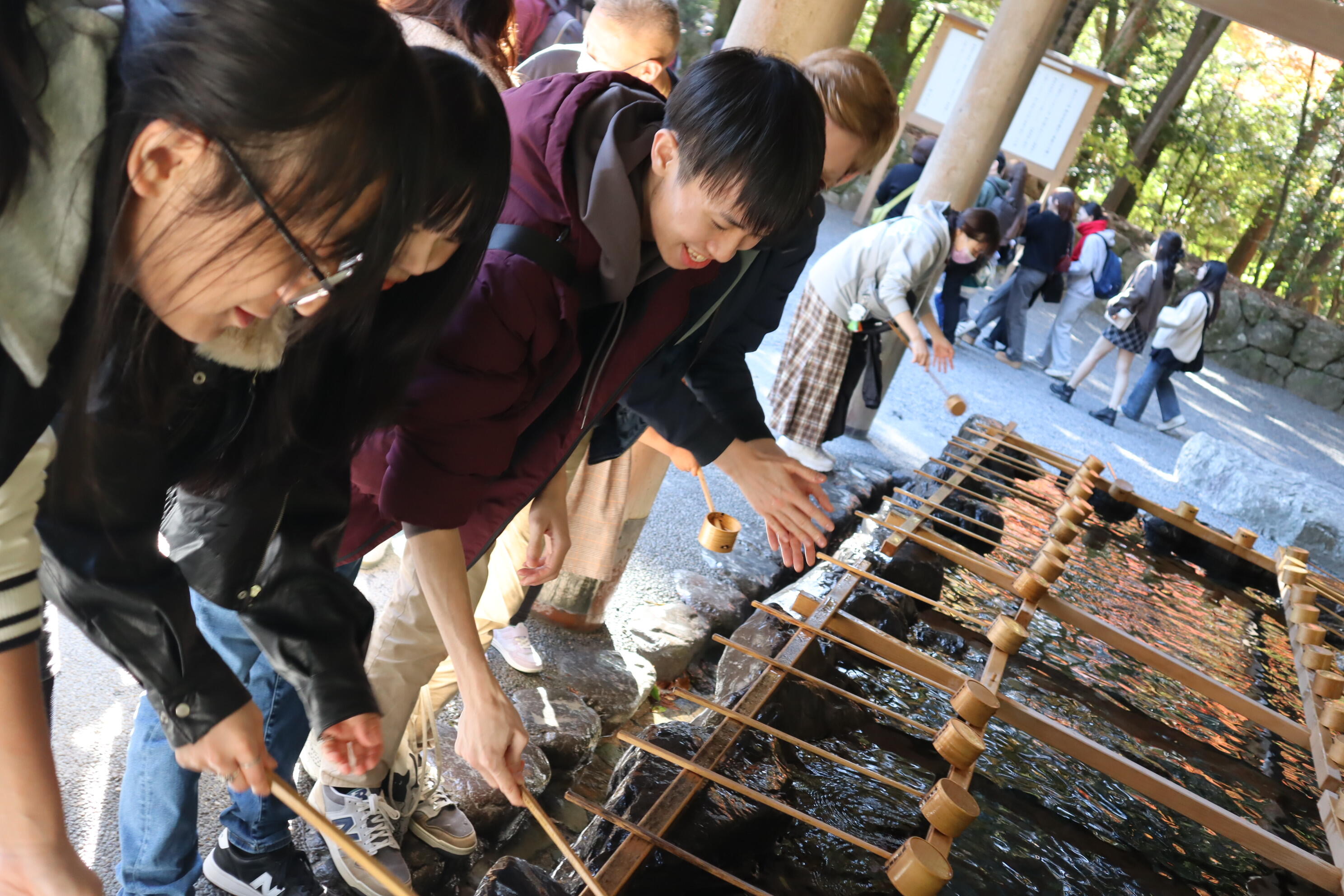 手水舎で手の清め方を説明する学生