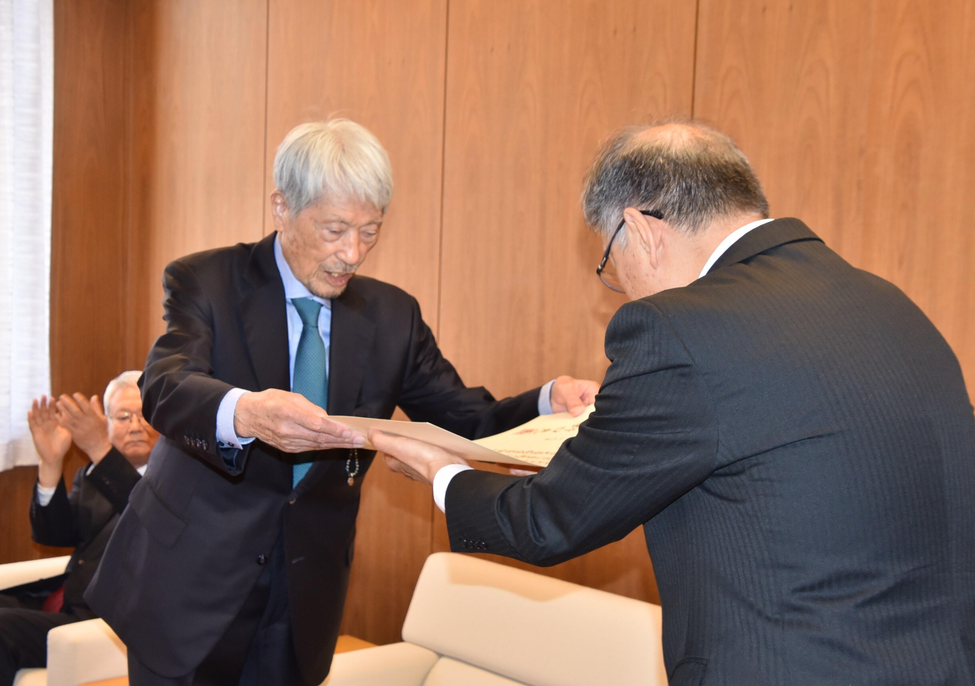 野口学長（右）から名誉学位記を手渡される長谷川顧問