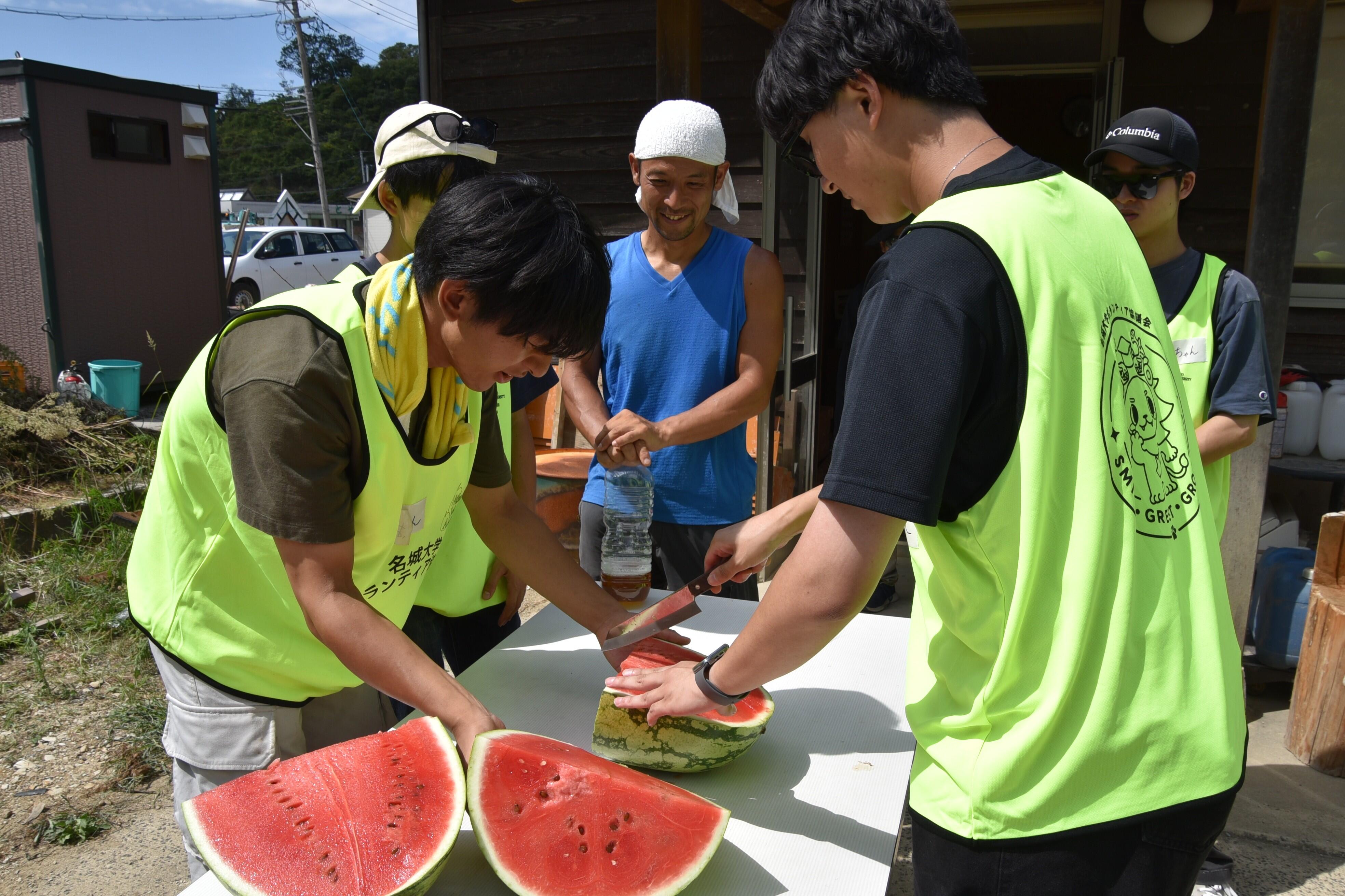 大石さんと話しながら差し入れのスイカを切る学生たち