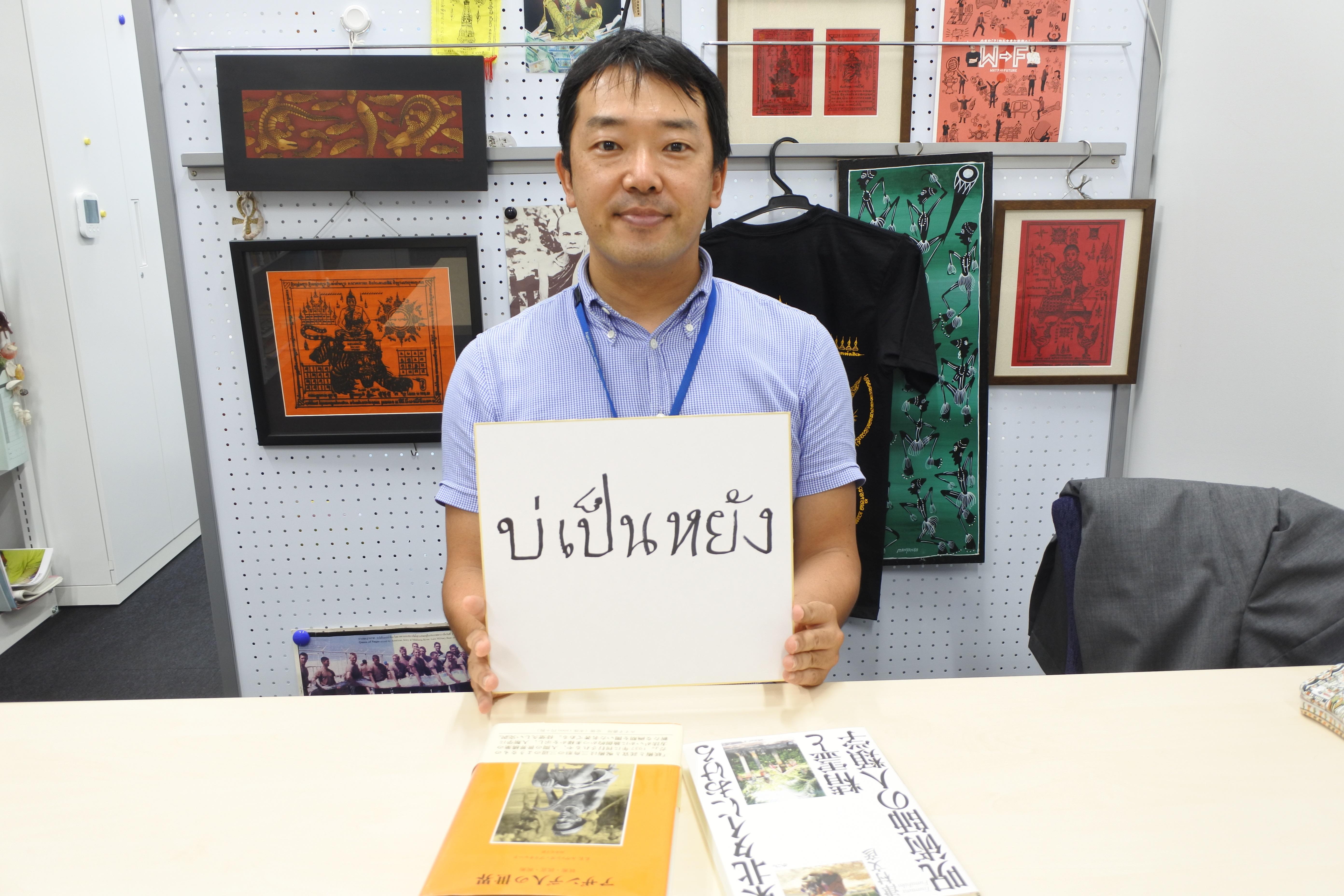 呪布（右肩の後ろ）を背に、東北タイの方言を書いた色紙を手にする津村文彦教授