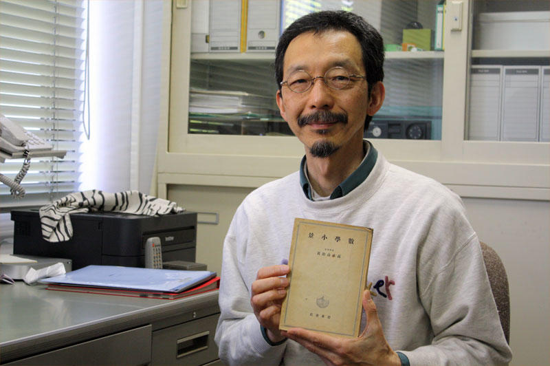 「名城大学の数学科には素晴らしい先生方がそろっています」と語る小澤教授。手にしているのは小学生時代に読んだ『数学小景』